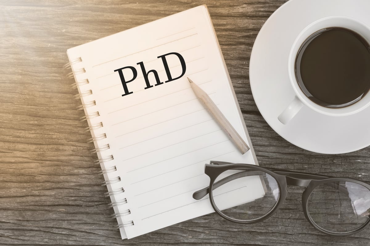 Concept PhD Doctor of  Philosophy Degree Education Graduation message on notebook with glasses, pencil and coffee cup on wooden table.